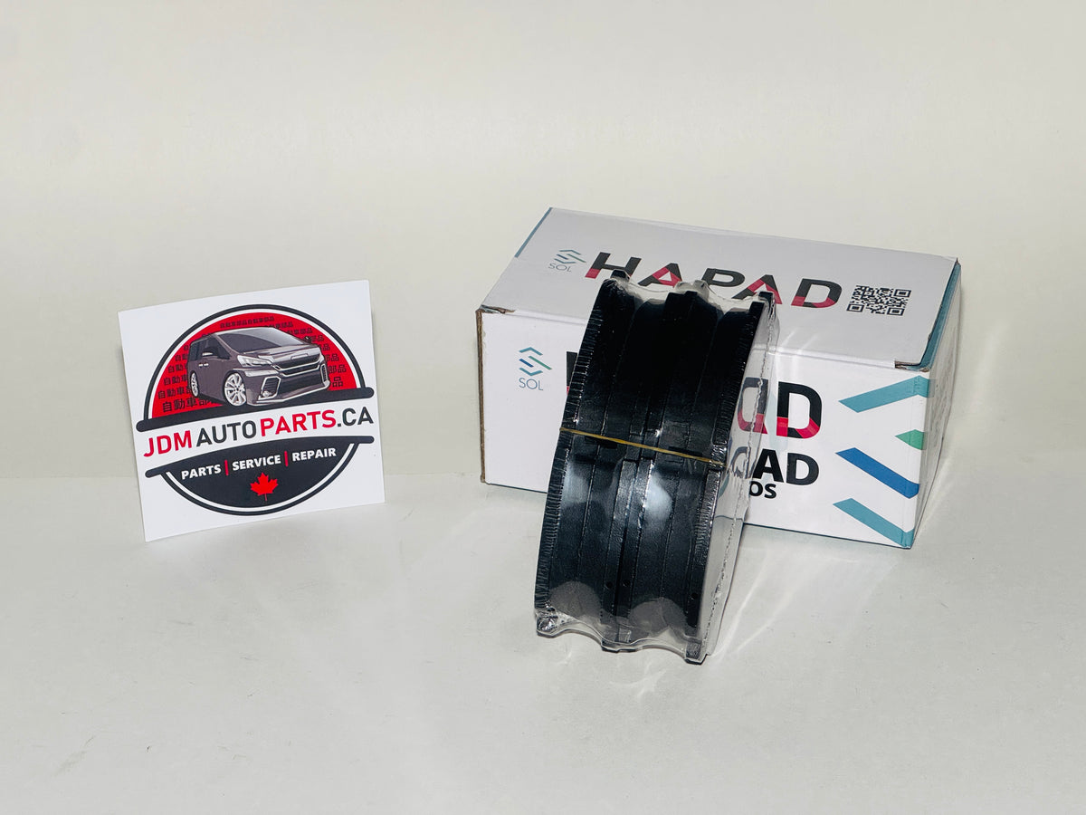 A black spool of HAPAD Load Mods performance tire compound placed in front of its white retail box, with a JDM Auto Parts card on a plain light background.