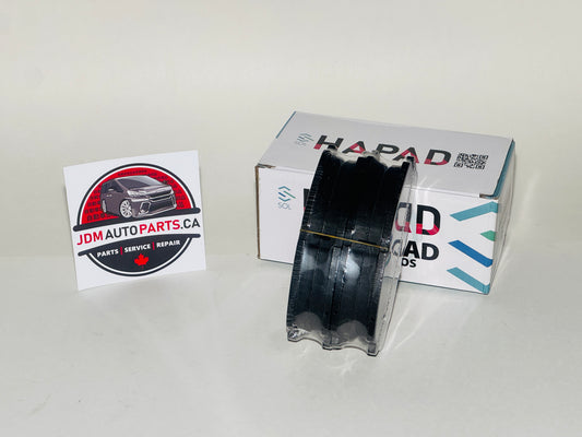 A black spool of HAPAD Load Mods performance tire compound placed in front of its white retail box, with a JDM Auto Parts card on a plain light background.