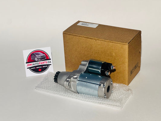 Car starter motor on bubble wrap with cardboard box and 'JDM Auto Parts' sign in the background