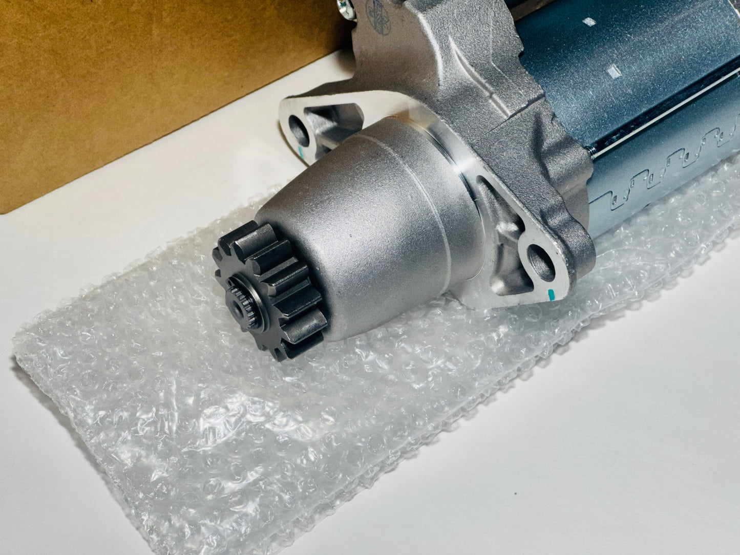 Car starter motor on a white surface with clear plastic wrap