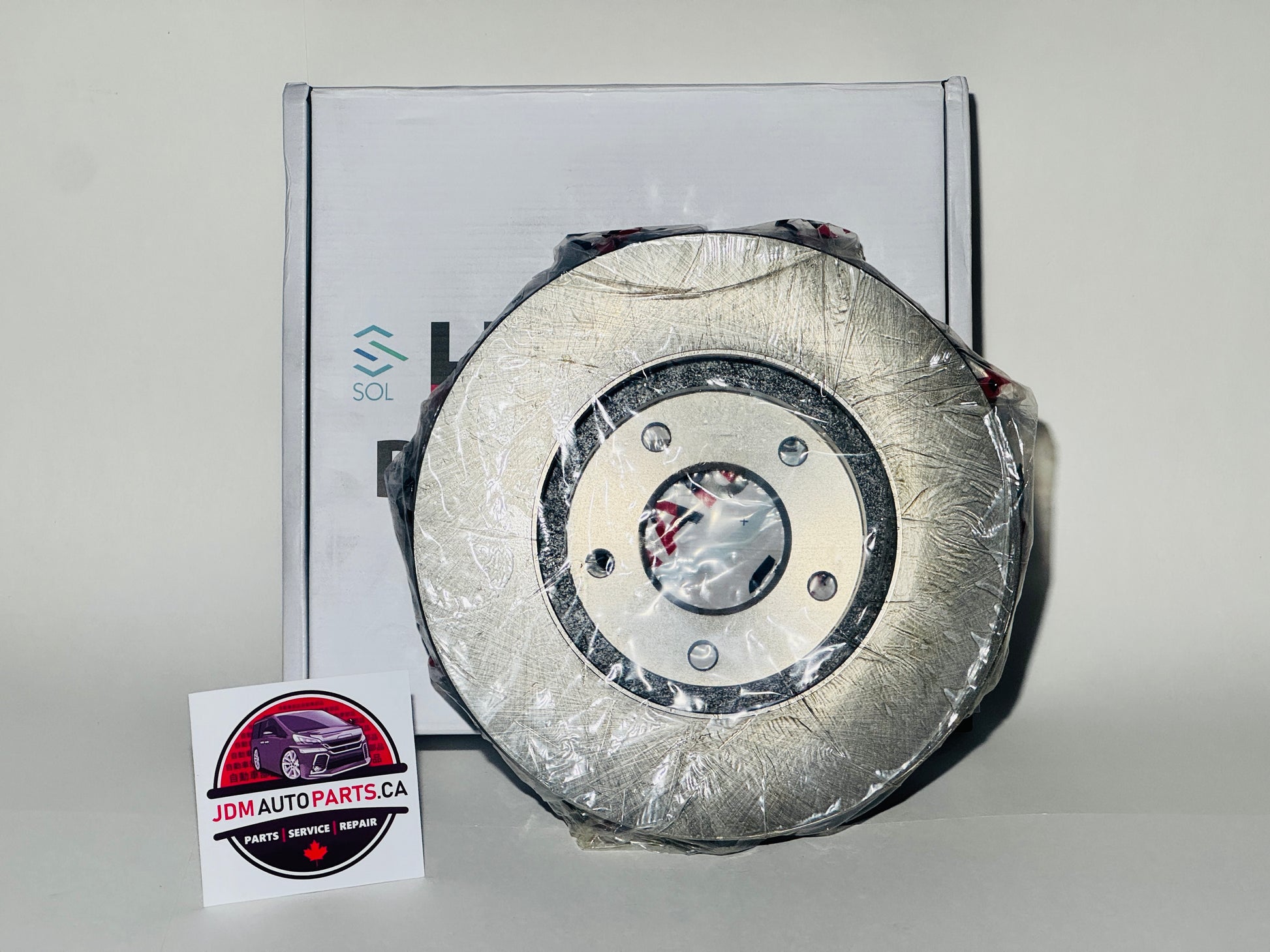 A new brake rotor packaged in plastic, displayed in front of a box with a label indicating the product is for a Nissan Elgrand E51 series.