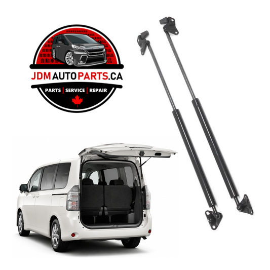 A pair of black gas strut suspension lifters shown next to a white minivan with its rear hatch open, on a white background. A circular logo for 'JDM AUTO PARTS.