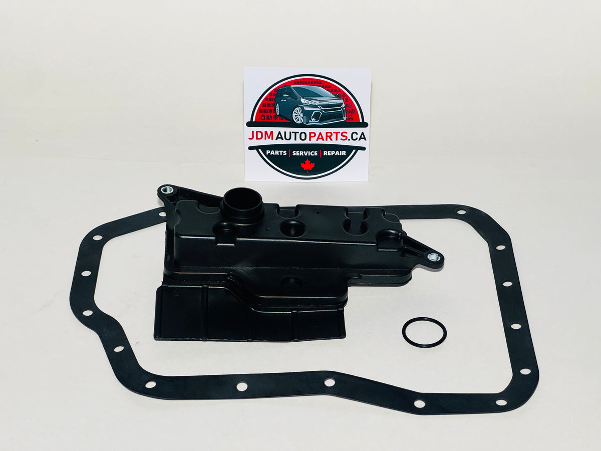 A black plastic automotive transmission filter and gasket set with a large outer gasket, a central filter, and a small O-ring, displayed on a light background with a JDM Auto Parts logo card behind it.