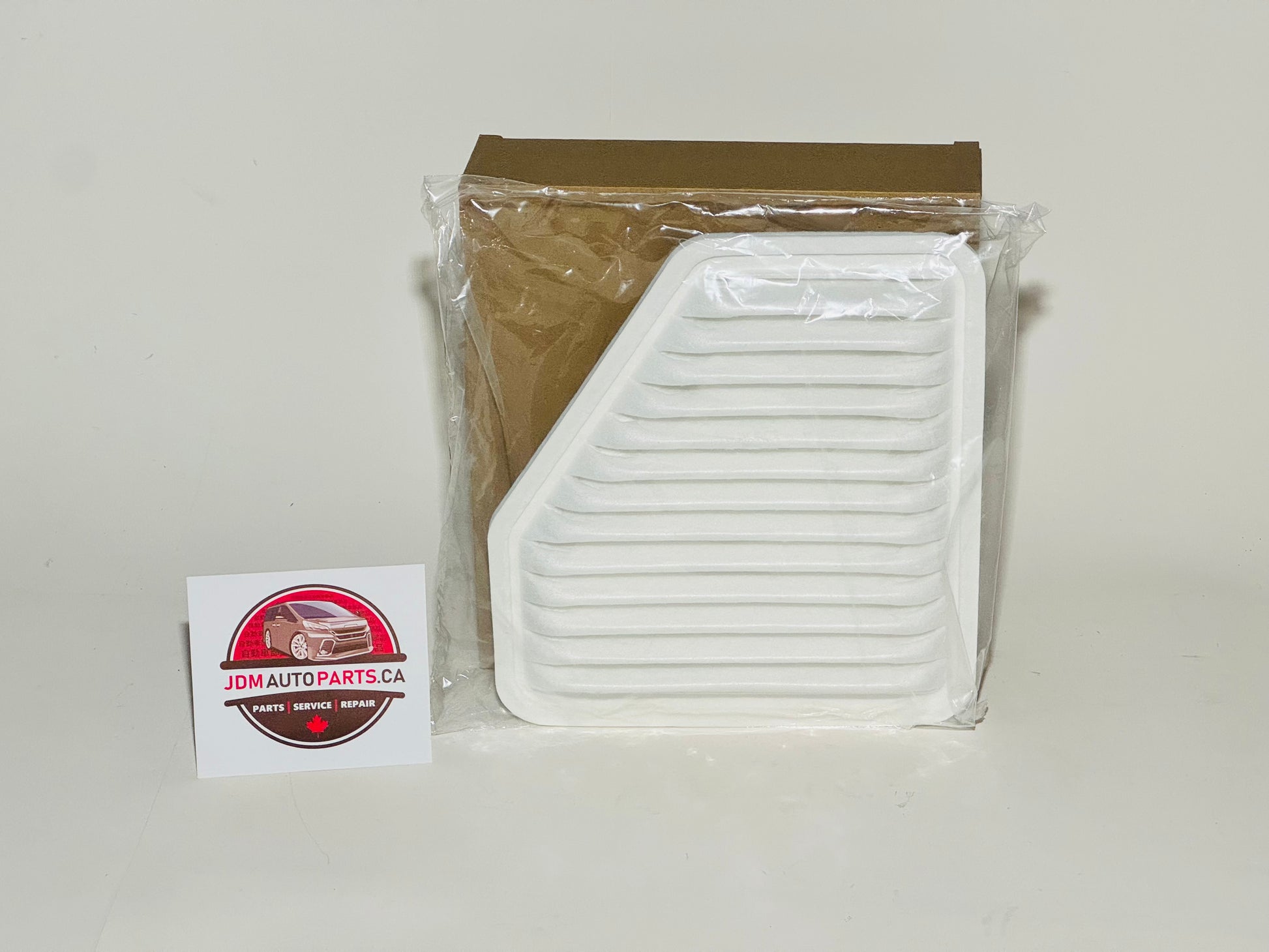 A white engine air filter for Toyota vehicles, placed in front of its packaging, with a Toyota logo sticker next to it.