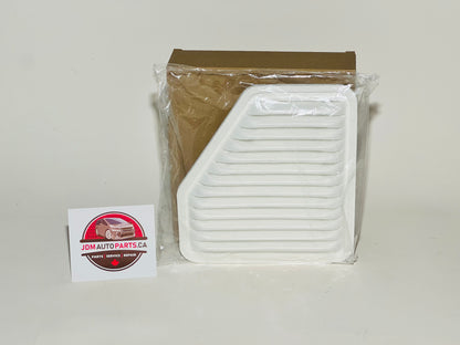 A white engine air filter for Toyota vehicles, placed in front of its packaging, with a Toyota logo sticker next to it.